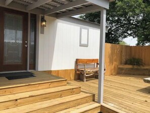 Una terraza de madera con escalones que conducen a una puerta, un banco y una valla de madera al fondo.