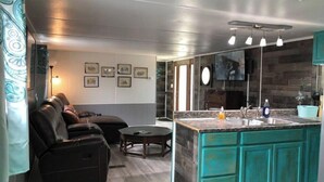 Eine moderne Küche mit einer zentralen Kochinsel, ein Essbereich mit Sofa und Tisch, sowie ein Wohnbereich mit Couch und Couchtisch.