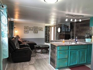 Relax in a stylish living area with a leather sofa and small table, surrounded by framed pictures, and a modern kitchen with a central island and sink.