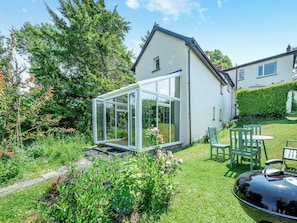 A house with a glass conservatory, a lawn, and outdoor furniture. - Tan y Castell Cottage (Llanmill, near Narberth)