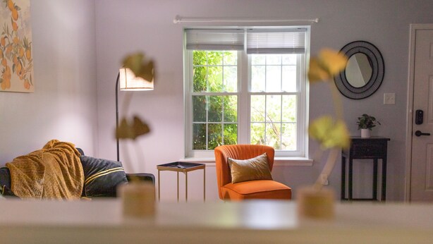 A living room with a sofa, a chair, a small table, a floor lamp, and a window with blinds.