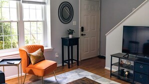 A living room with a sofa, a TV stand, a door, and a window with blinds.