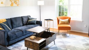 A modern living room with a dark blue sofa, an orange armchair, a wooden coffee table, and a floor lamp.