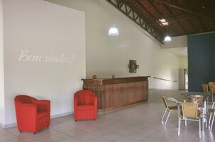 Un área de recepción con un mostrador de madera, dos sillones rojos y una zona de estar con sillas de mimbre y una mesa.