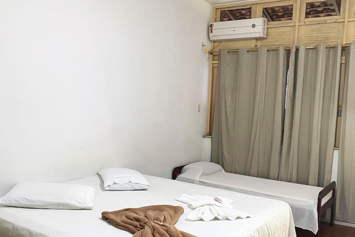 A hotel room with two single beds, a wooden headboard, a window with curtains, and an air conditioning unit.