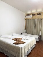 Una habitación de hotel con dos camas individuales, un cabecero de madera, una ventana con cortinas y un equipo de aire acondicionado.