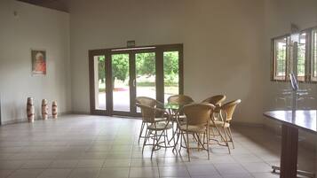 Una habitación amplia con un gran ventanal corredero que da a un espacio exterior, sillas de mimbre dispuestas alrededor de una mesa, y un cuadro en la pared.