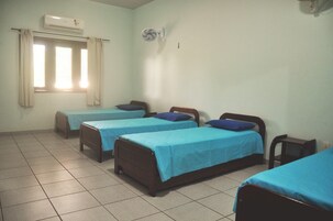 Una habitación con cuatro camas individuales, una ventana con cortinas, aire acondicionado y un ventilador de pared.