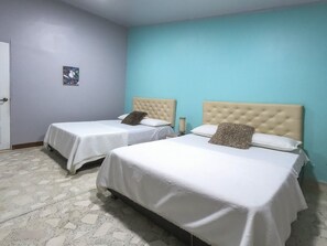 A hotel room with two beds, each with a tufted headboard, white bedding, and a small bedside table with a lamp.