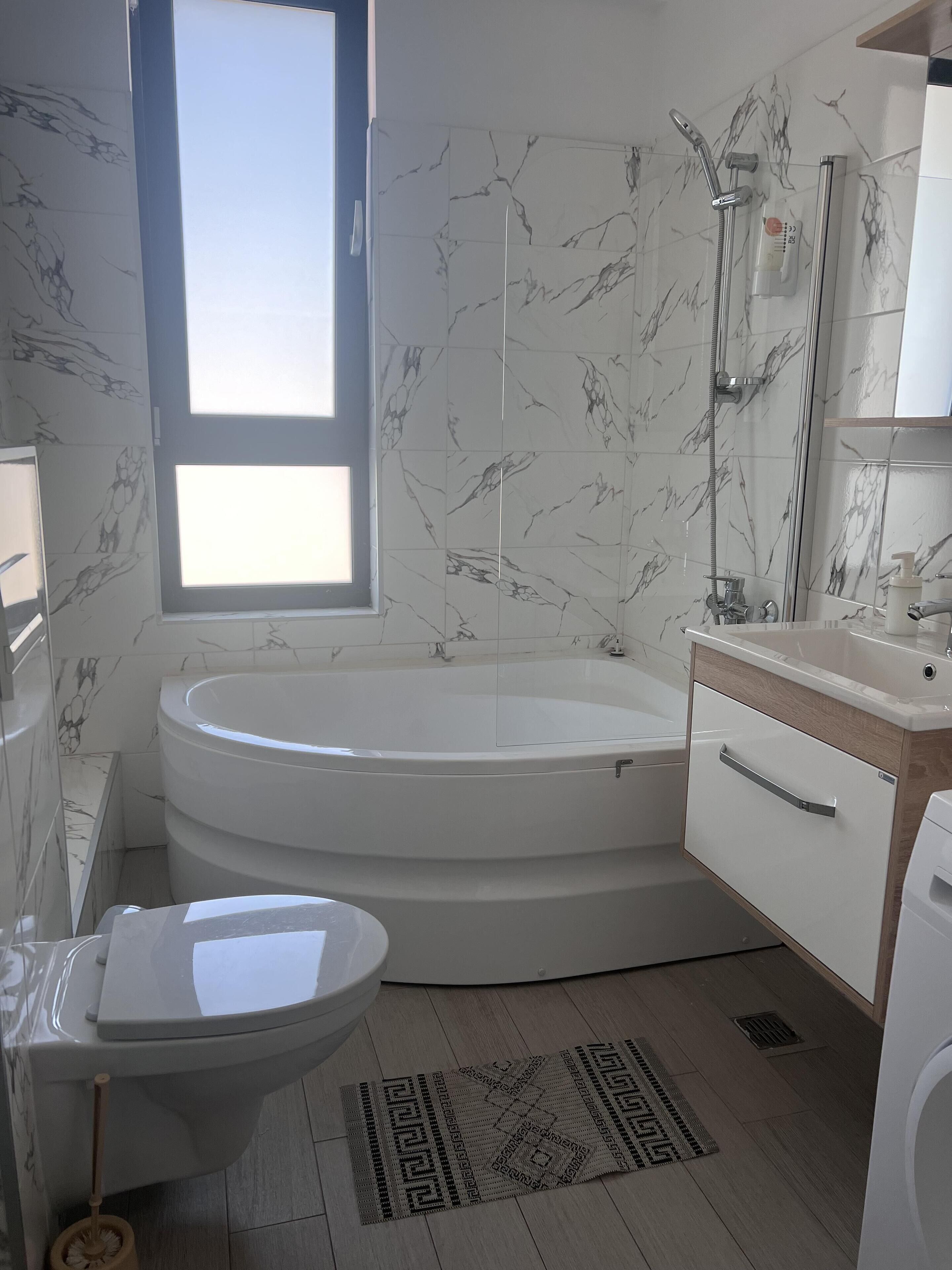 A bathroom with a bathtub, toilet, and sink, featuring marble walls and a window.