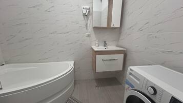 A bathroom with a bathtub, a sink, a mirror, and a washing machine.