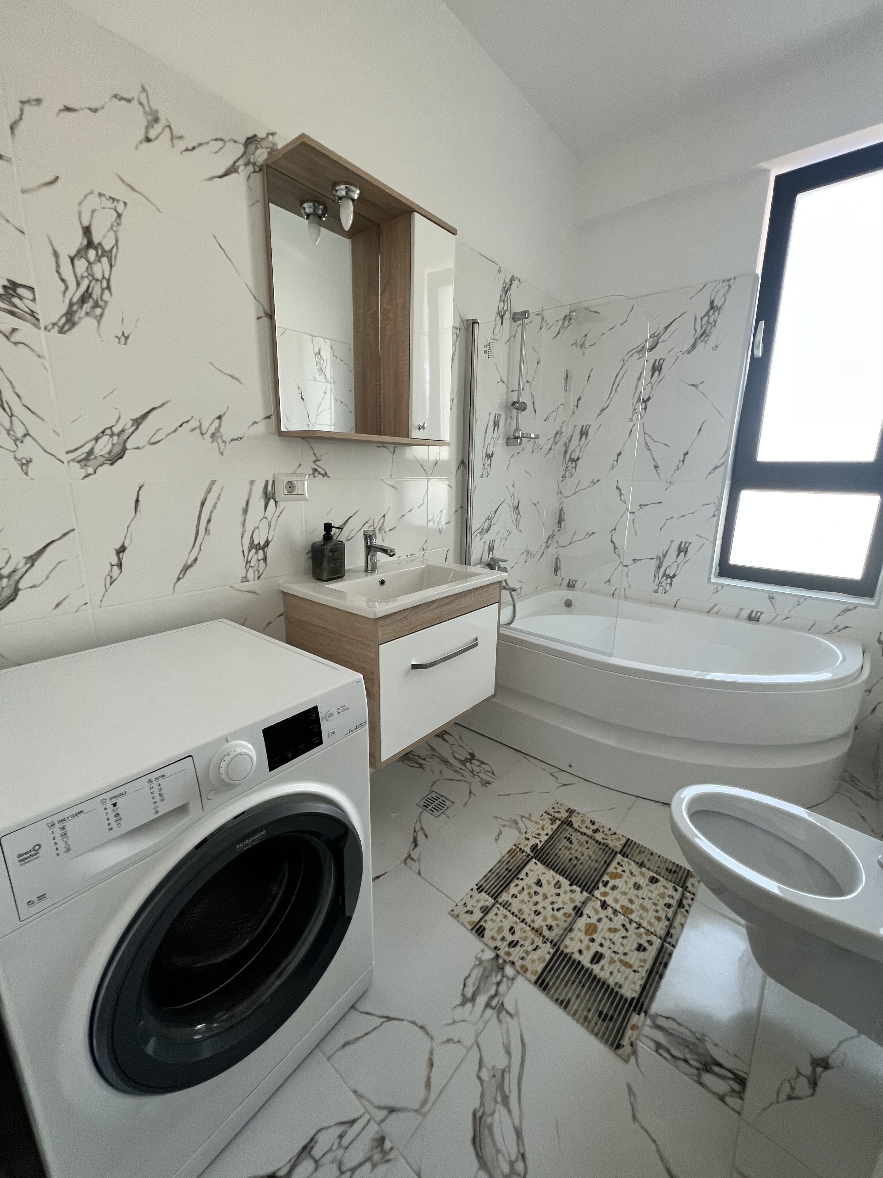 A modern bathroom with a built-in washing machine, a bathtub, and a toilet.