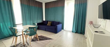 Una sala de estar moderna con comedor, que incluye un sofá, un televisor y una mesa de comedor con sillas.