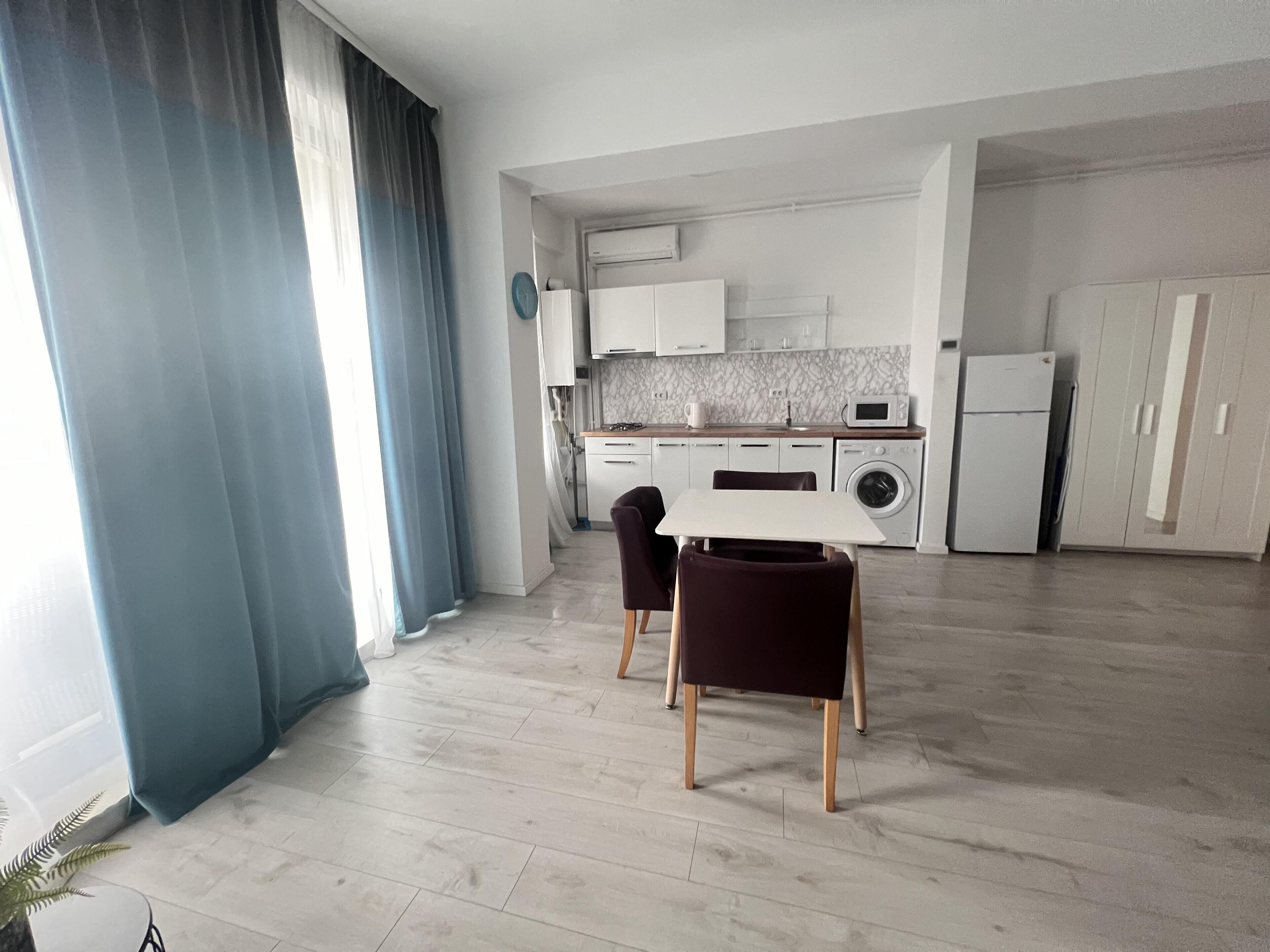 Une cuisine moderne avec des meubles blancs, un four encastré et un lave-linge. On y trouve également un coin repas avec une table et des chaises.