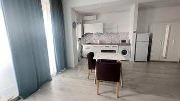 Une cuisine moderne avec des meubles blancs, un four encastré et un lave-linge. On y trouve également un coin repas avec une table et des chaises.