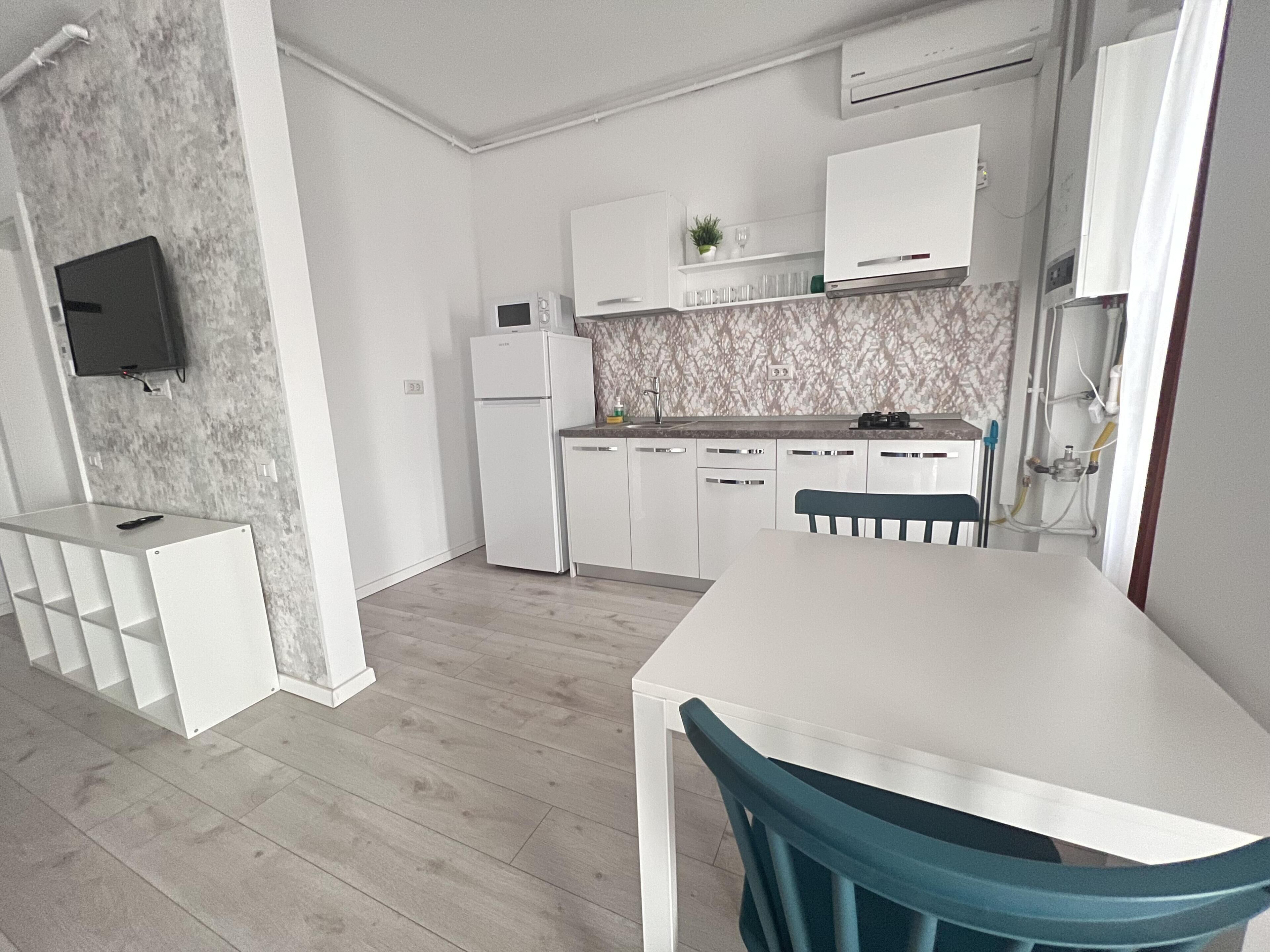 A modern kitchen with white cabinetry, a built-in microwave, and a dining area with a white table and teal chairs.
