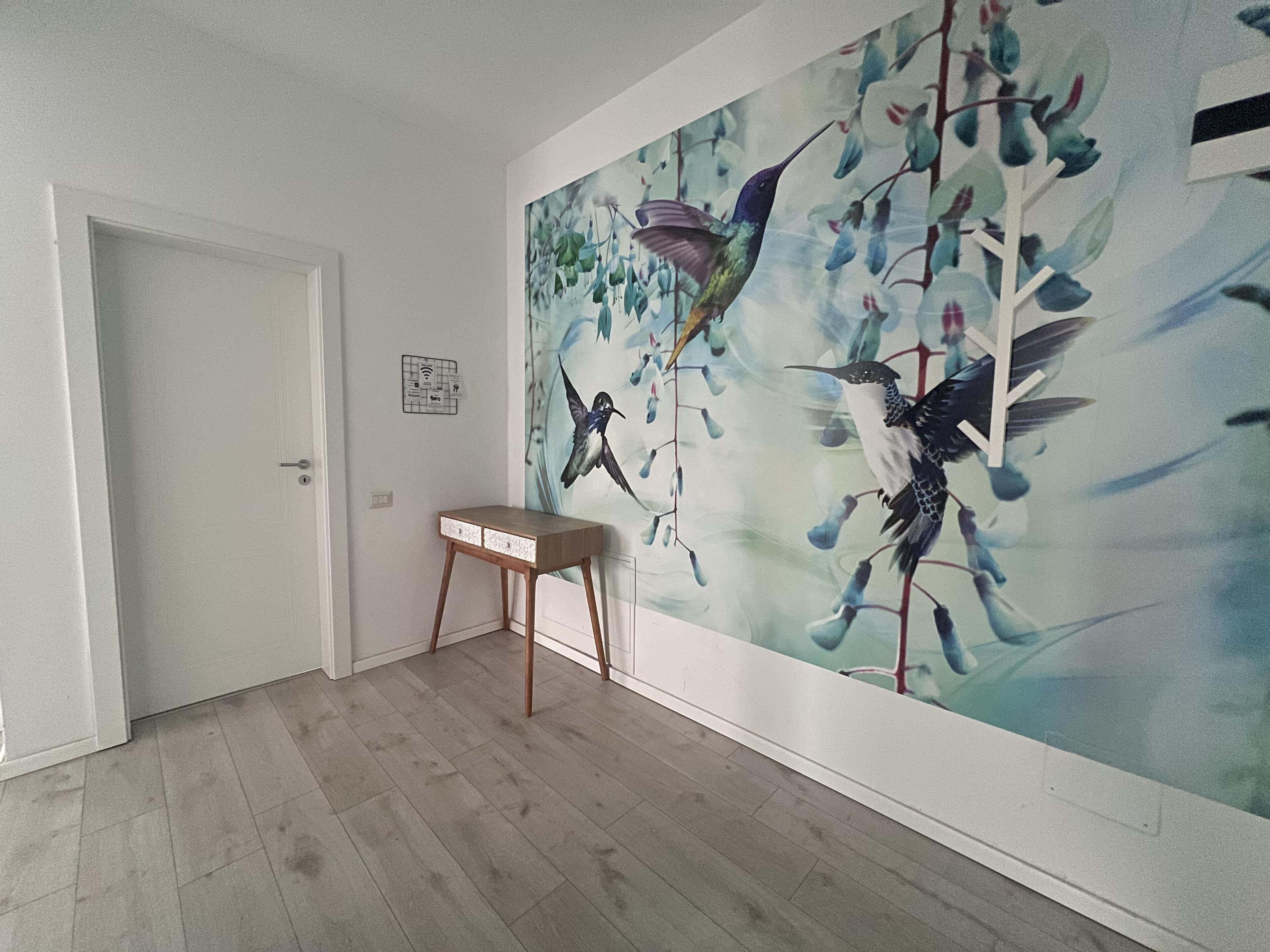 A room with a wooden floor, a white door, and a wall mural of birds on branches.