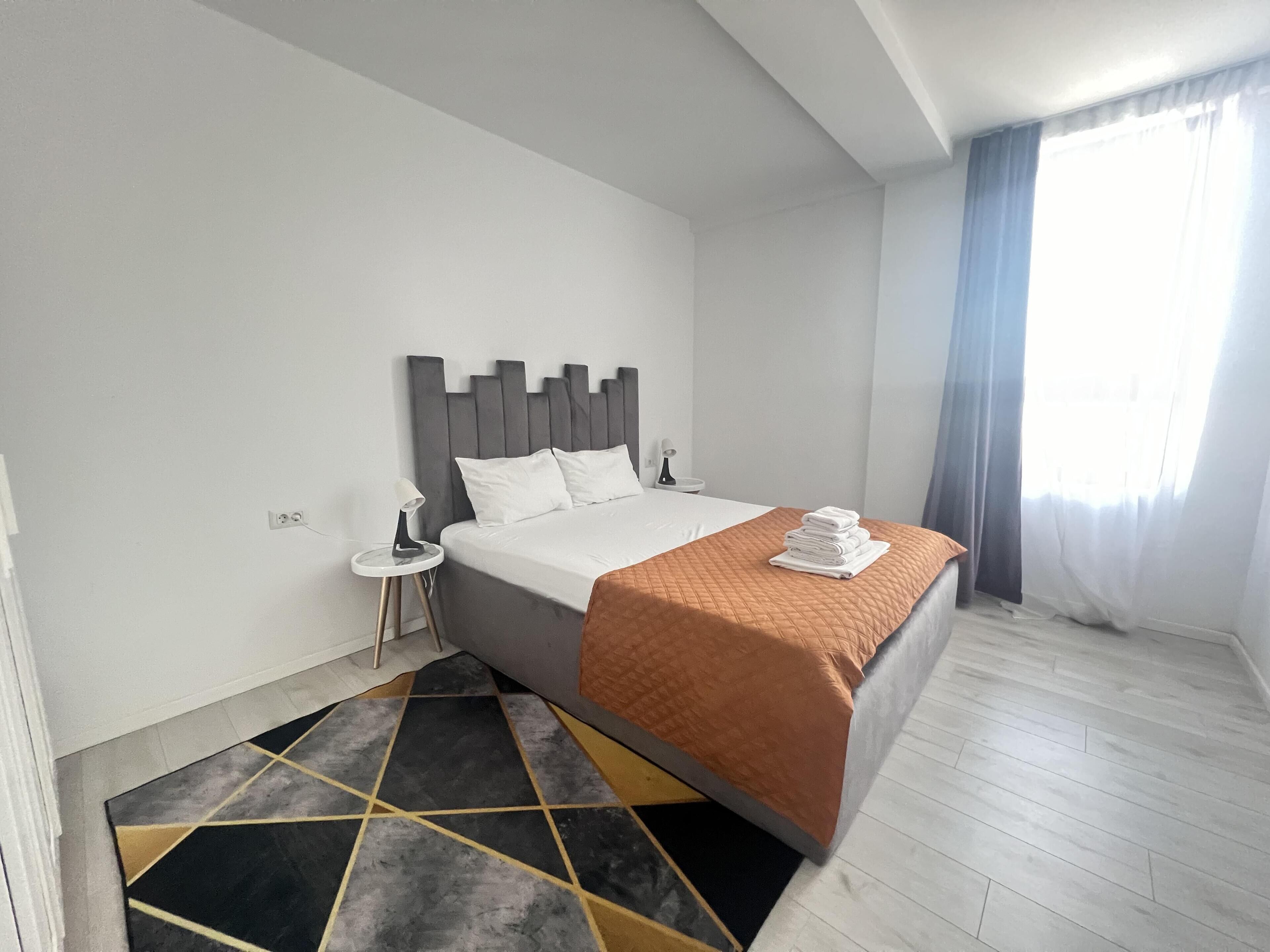 Habitación de hotel moderna con una cama grande, una mesita de noche pequeña y vistas al exterior.