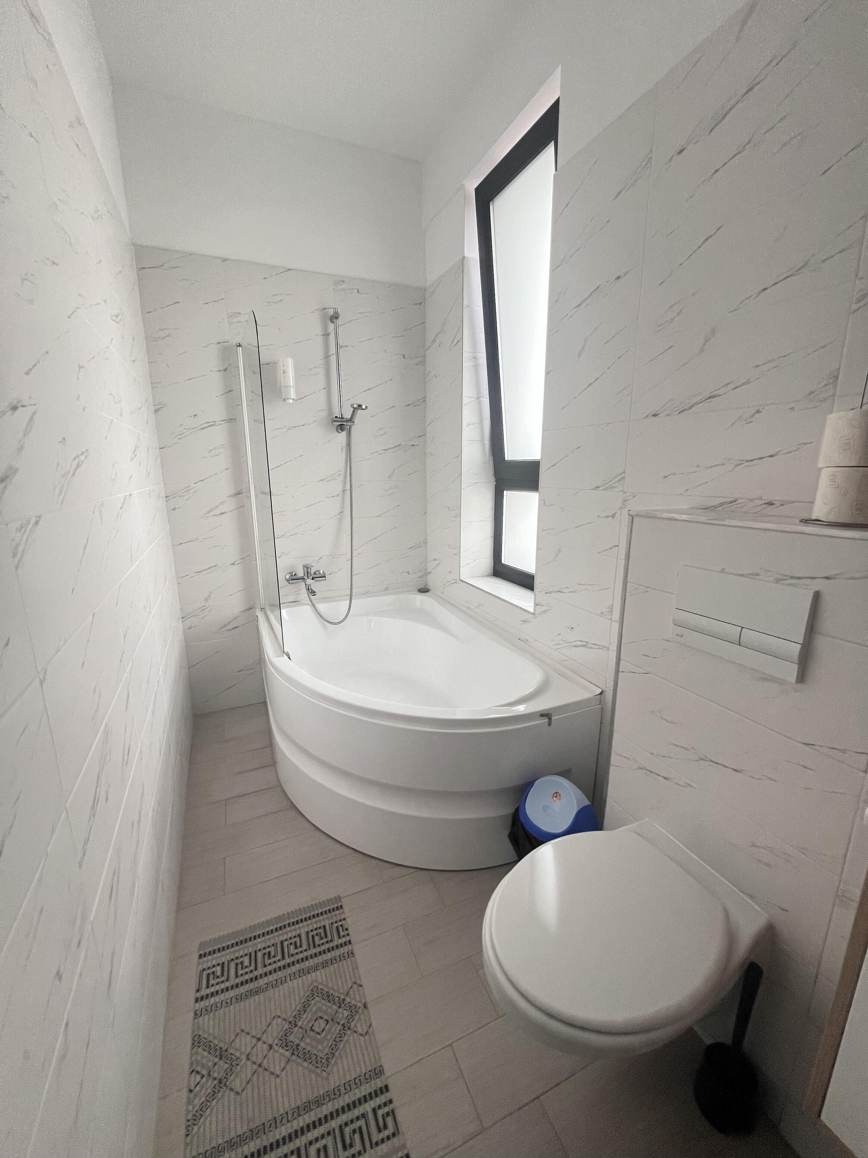 A bathroom with a bathtub, toilet, and a window.