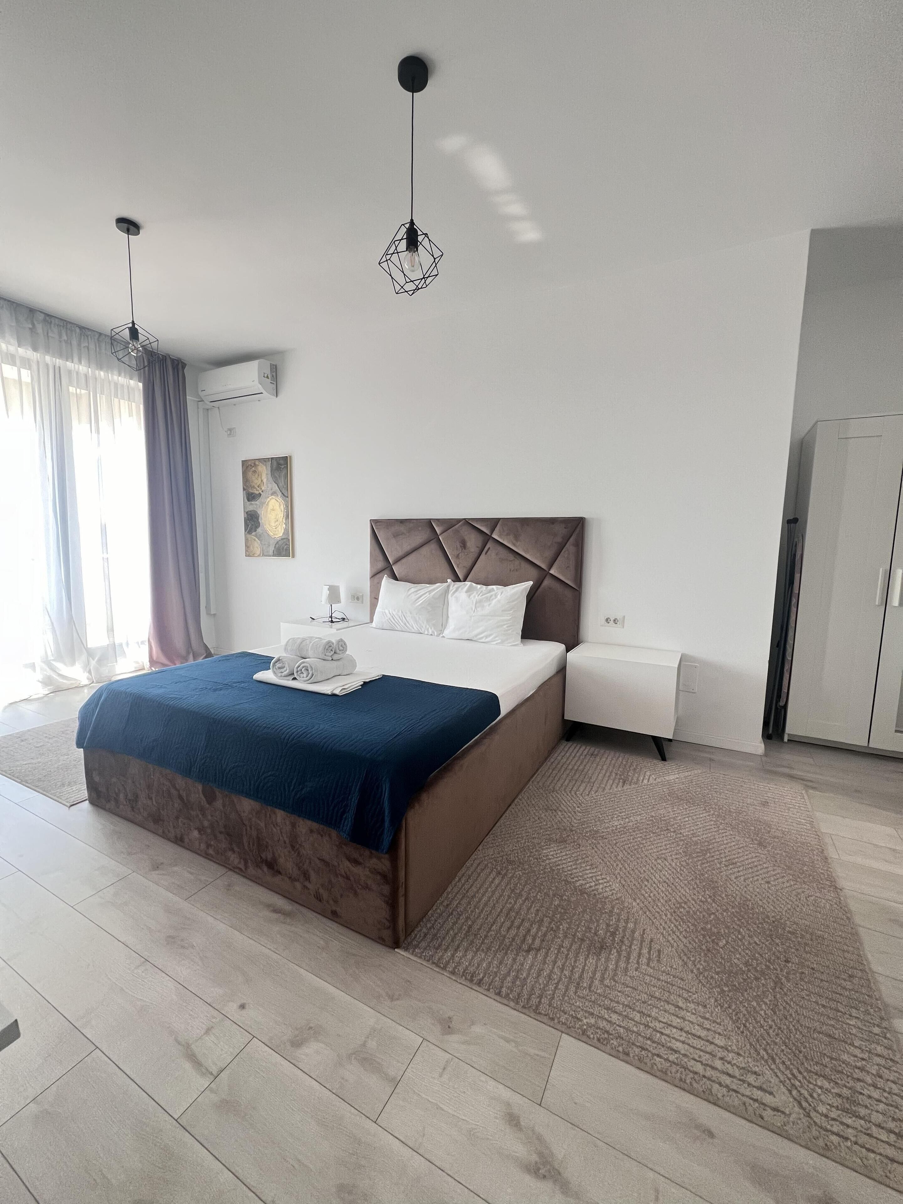 A modern hotel room with a large bed, a bedside table, a wardrobe, and a hanging light fixture.