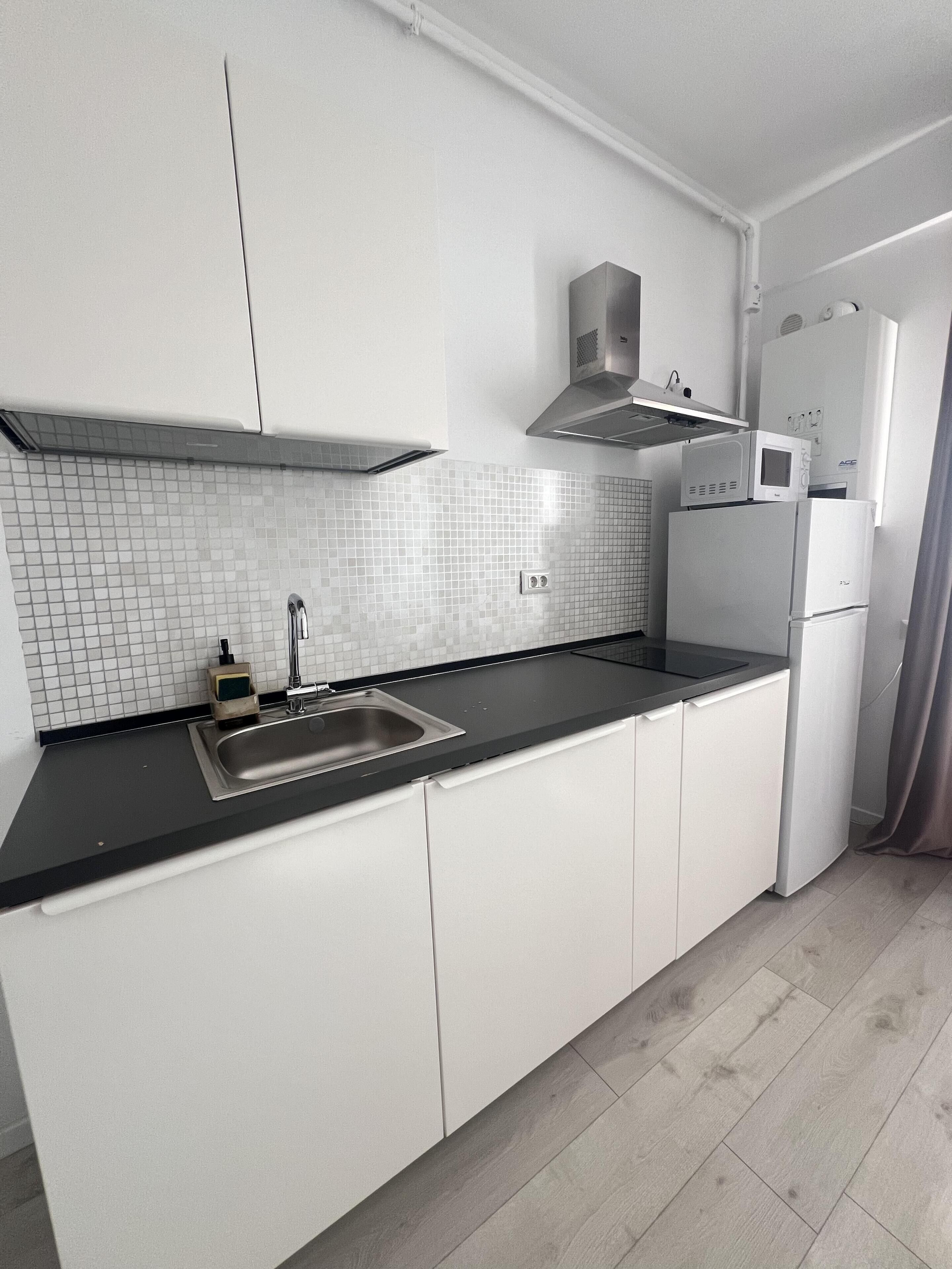 A modern kitchen with white cabinets, a black countertop, a stainless steel sink, a microwave, and a refrigerator.
