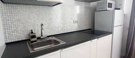 A modern kitchen with white cabinets, a black countertop, a stainless steel sink, a microwave, and a refrigerator.
