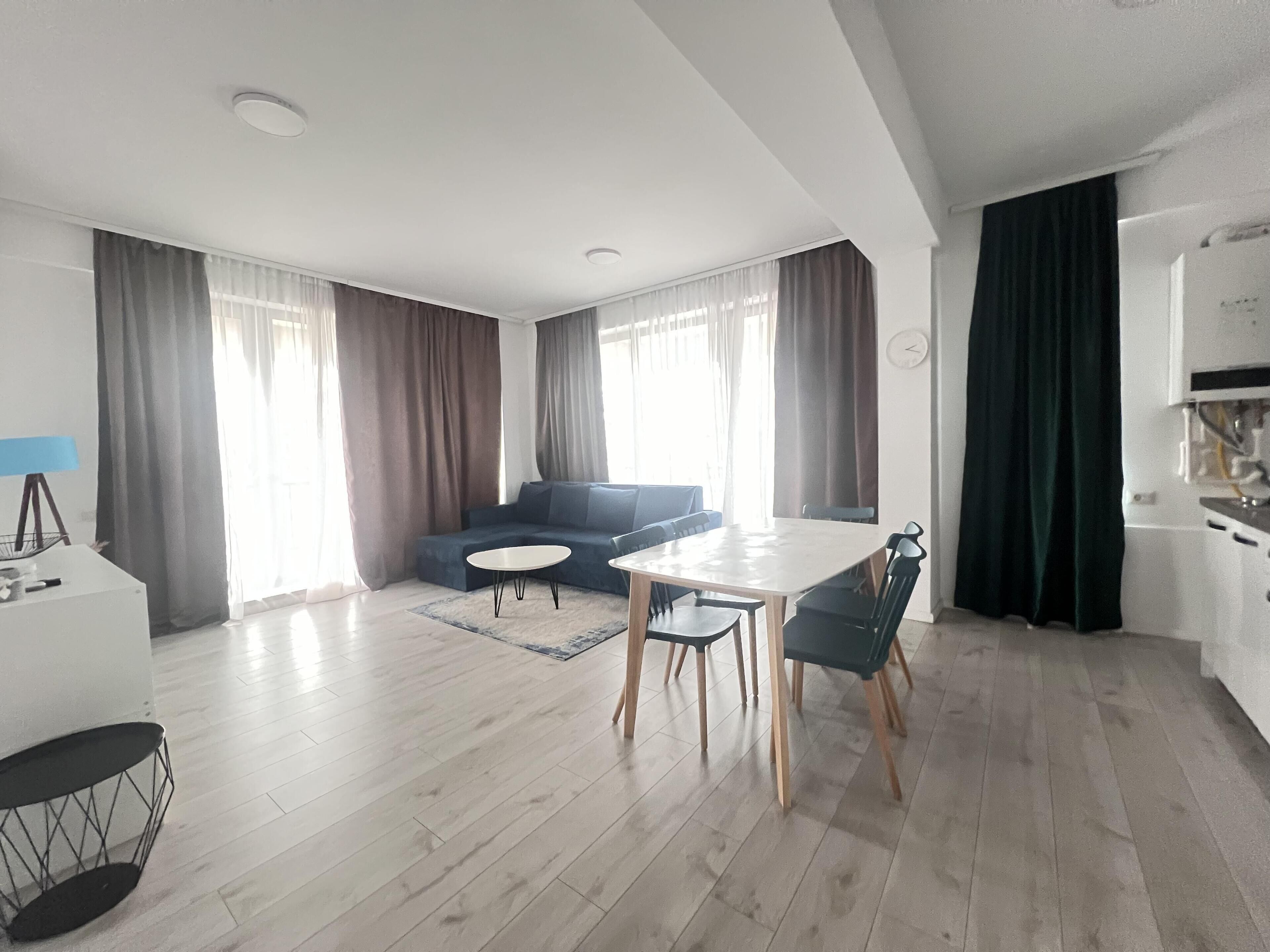 Un salon moderne avec un canapé bleu, une table à manger avec des chaises et un coin cuisine équipé d’une cuisinière.