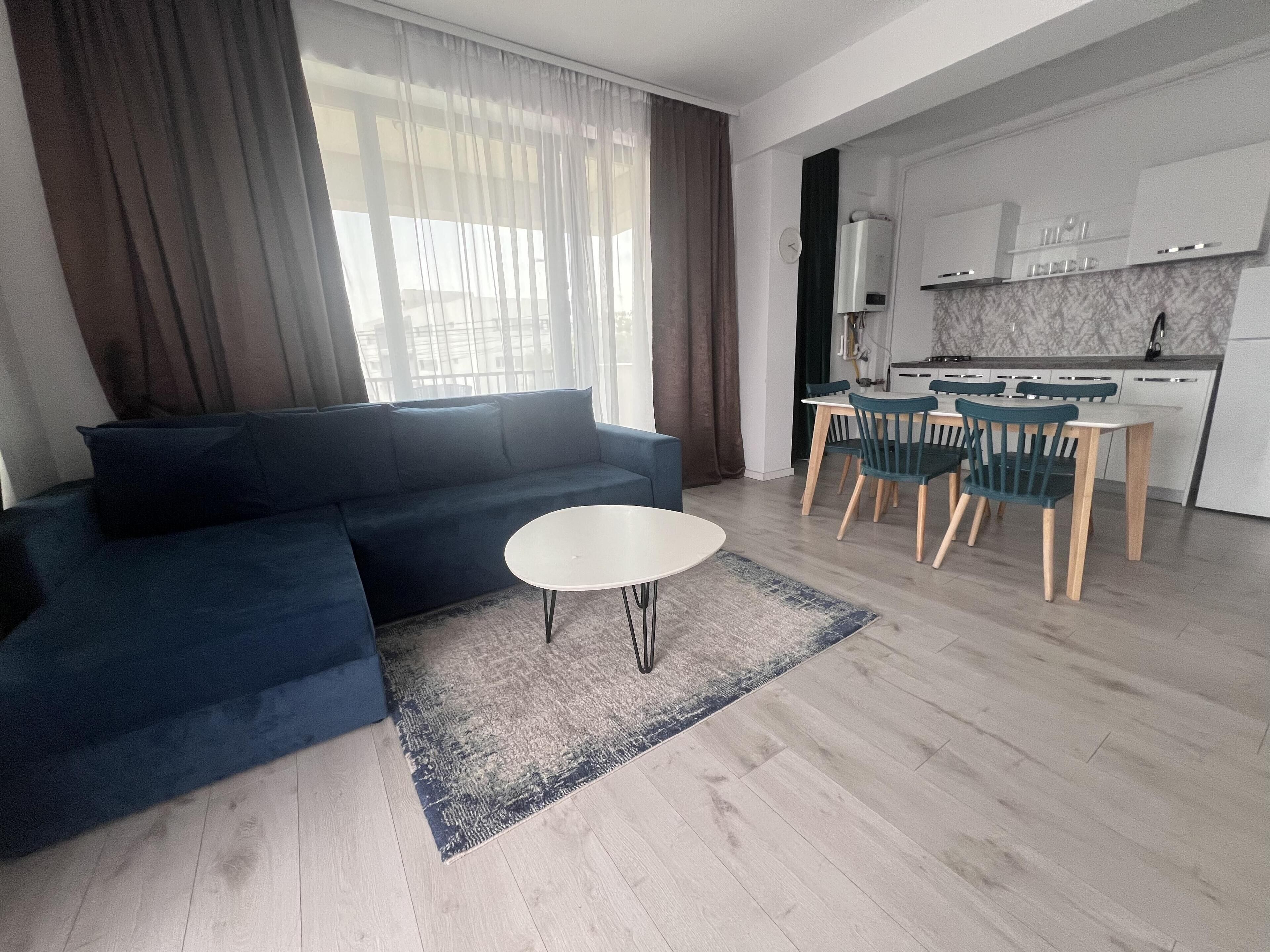Un salon moderne avec un canapé bleu, une table basse ronde et un coin repas comprenant des chaises en bois et une table blanche.