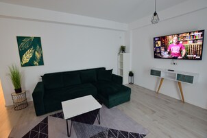 Una sala de estar moderna con un sofá seccional verde oscuro, una mesa de centro blanca y un televisor de pantalla plana montado en la pared.