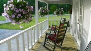 Eine Veranda mit Schaukelstuhl, weißen Geländern und blumengeschmückten Körben.