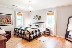 Un dormitorio con cama, mesita de noche, cómoda, silla y un cuadro en la pared.