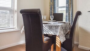 A dining area with a table set for two, two chairs, a window with blinds, and a curtain.