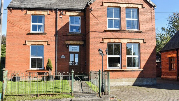 A red brick schoolhouse with a traditional gabled roof, a front door, and a small front garden.