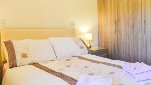 A bed with floral bedding, a bedside lamp, and a wooden wardrobe.