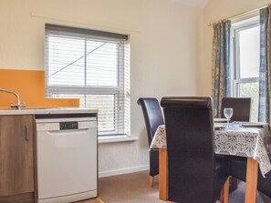 A compact kitchen with a dishwasher, a window with blinds, and a dining area with a table and chairs.