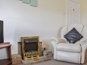 A living room with a television, a fireplace, a white leather armchair, and a door.