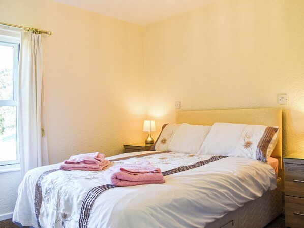 A neatly made bed with pink towels, a bedside lamp, and a window with curtains.
