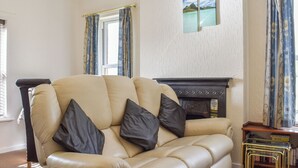 A beige leather sofa with black cushions, a fireplace, a window with curtains, and a bookshelf with books.