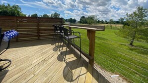 Une terrasse en bois avec une table et des chaises, donnant sur un champ verdoyant et des arbres.