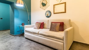 Uma sala de estar moderna com um sofá bege, almofadas estampadas, uma pequena mesa lateral e um abajur.