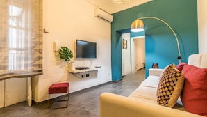 Uma sala de estar moderna com televisão de tela plana, um banco vermelho, uma parede em tom de verde-água e uma janela grande com cortinas leves.