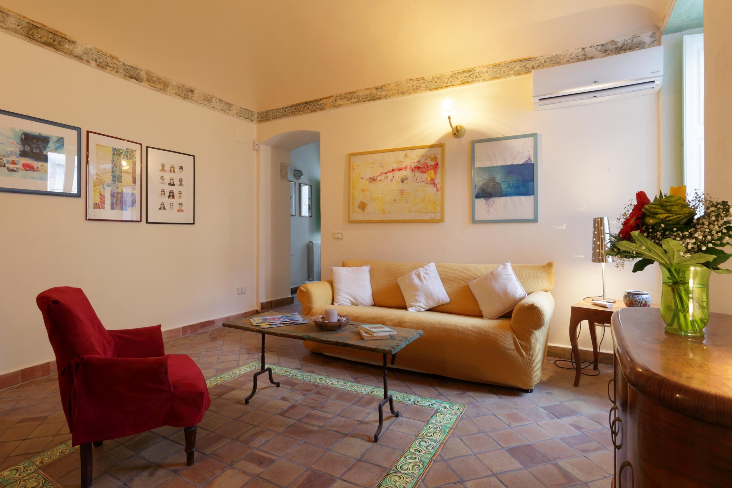 A living room with a red armchair, a beige sofa, a coffee table, and a vase with flowers.
