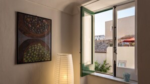 Une pièce avec une fenêtre, un tableau représentant des fruits accroché au mur et une grande lampe cylindrique.