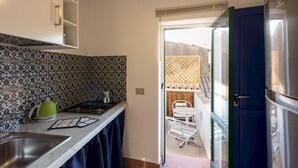 Une cuisine compacte équipée d’une cuisinière à gaz, d’un évier et d’une bouilloire verte. Une porte donne accès à un balcon avec une table et des chaises.