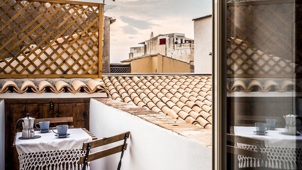 Un petit balcon avec une table et des chaises, une cloison en treillis de bois et une vue sur le paysage urbain.