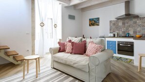 A living room with a sofa, a coffee table, a staircase, and a kitchen area with a stove and microwave. - Baroque Apartments - Dentrortigia (Syracuse)