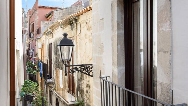 A narrow street with stone buildings, a metal balcony railing, and a hanging laundry line. - Baroque Apartments - Dentrortigia (Syracuse)