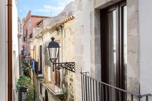 A narrow street with stone buildings, a metal balcony railing, and a hanging laundry line. - Baroque Apartments - Dentrortigia (Syracuse)