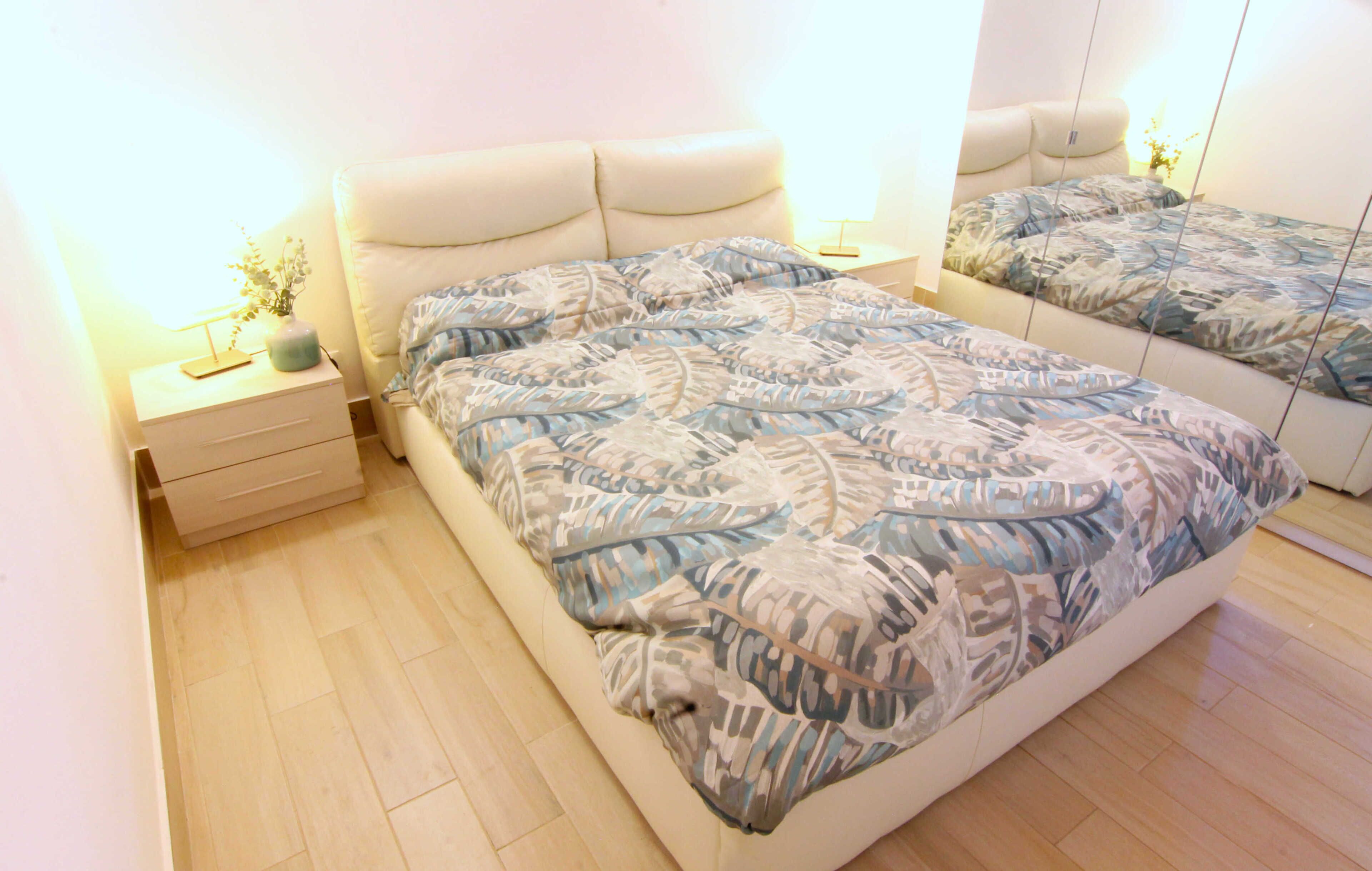 A bedroom with a bed, a nightstand, a mirror, and a bedside table.