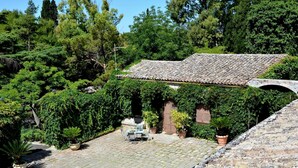 A stone building with a tiled roof, surrounded by lush greenery and a paved courtyard. - Villa de Leva - Casa Della Nonna (Modica)